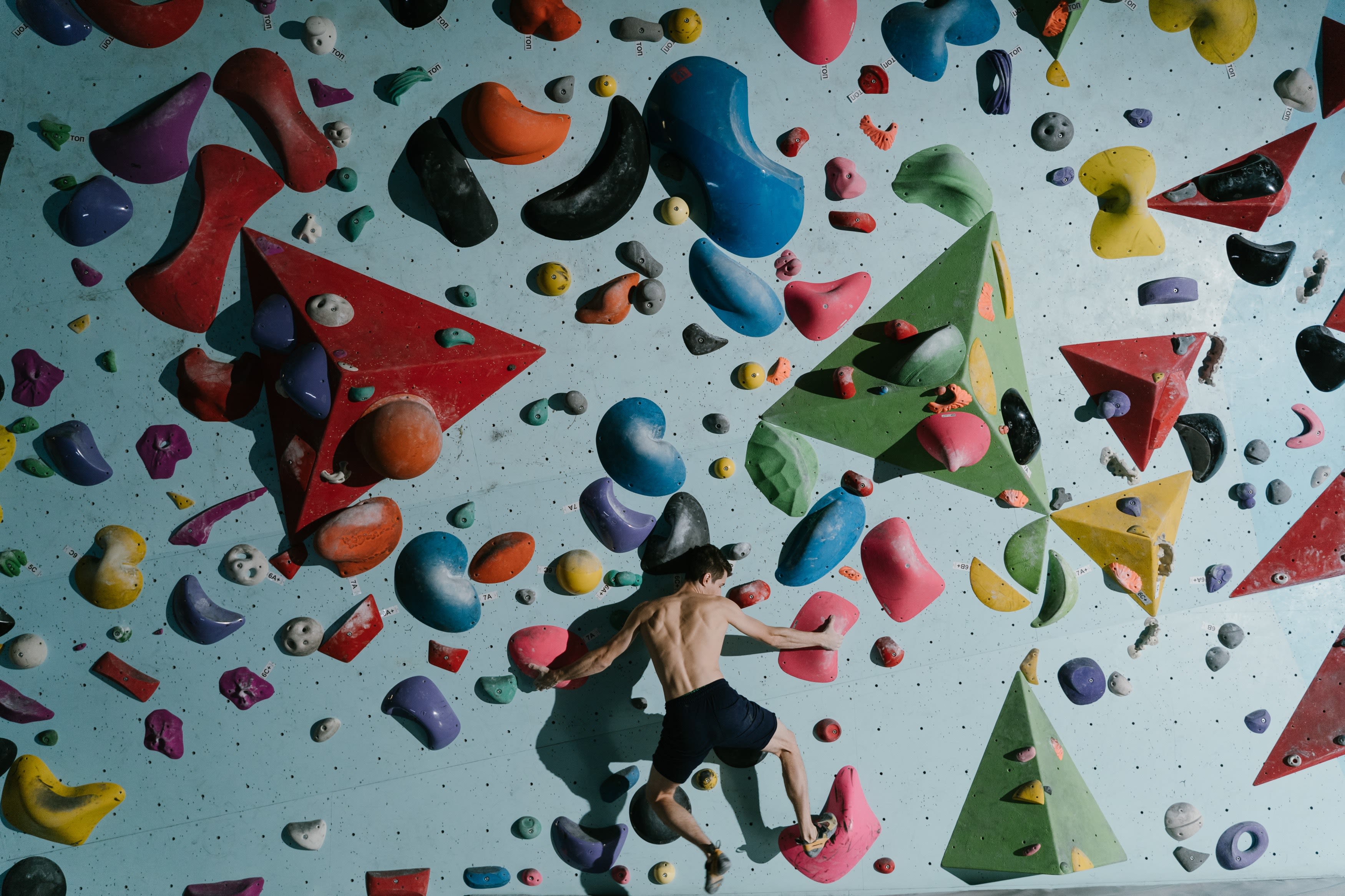 A man on a climbing wall, the wall is covered with different coloured climbing holds of various shapes and sizes.