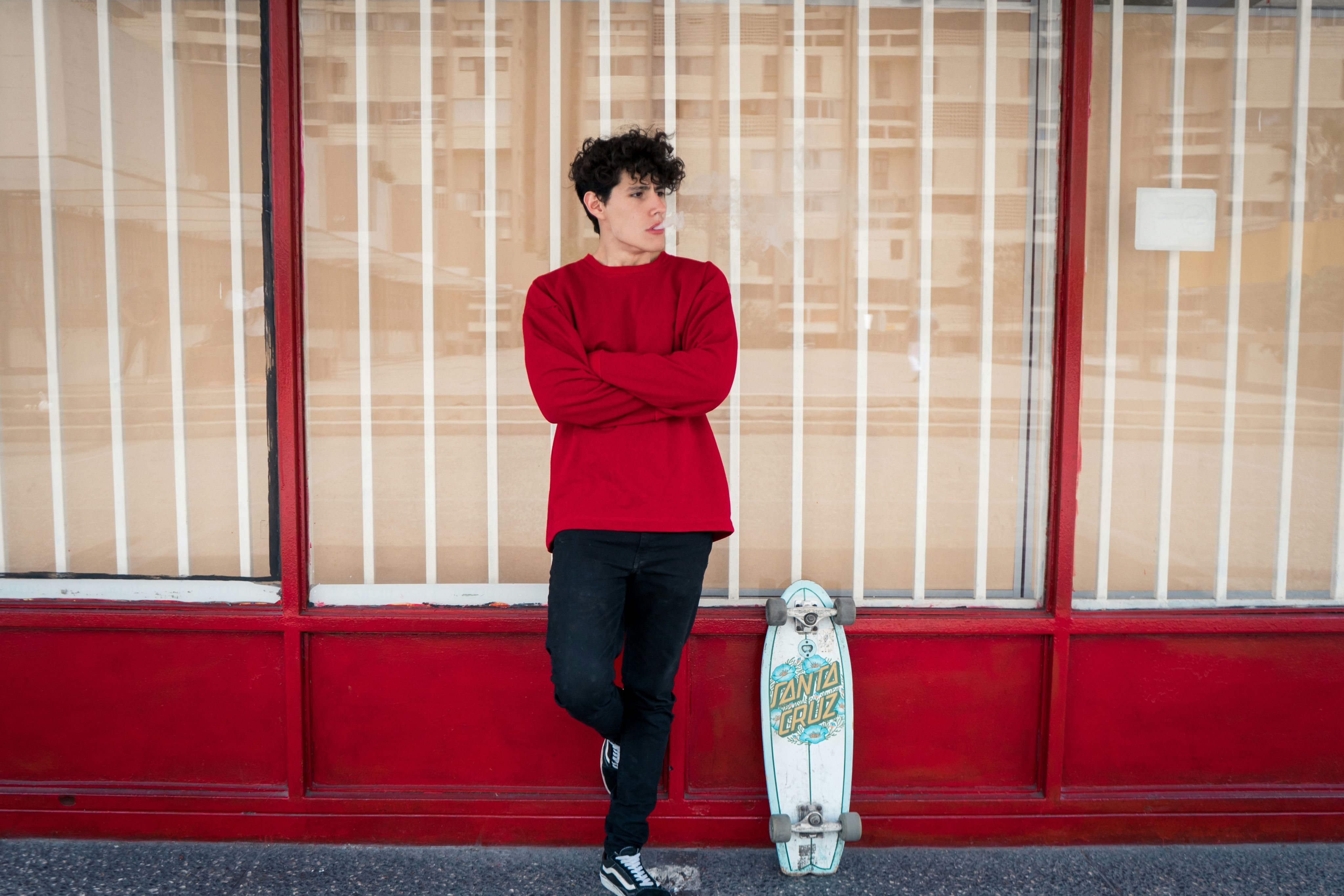 man leaning on glass wall beside leaning skateboard