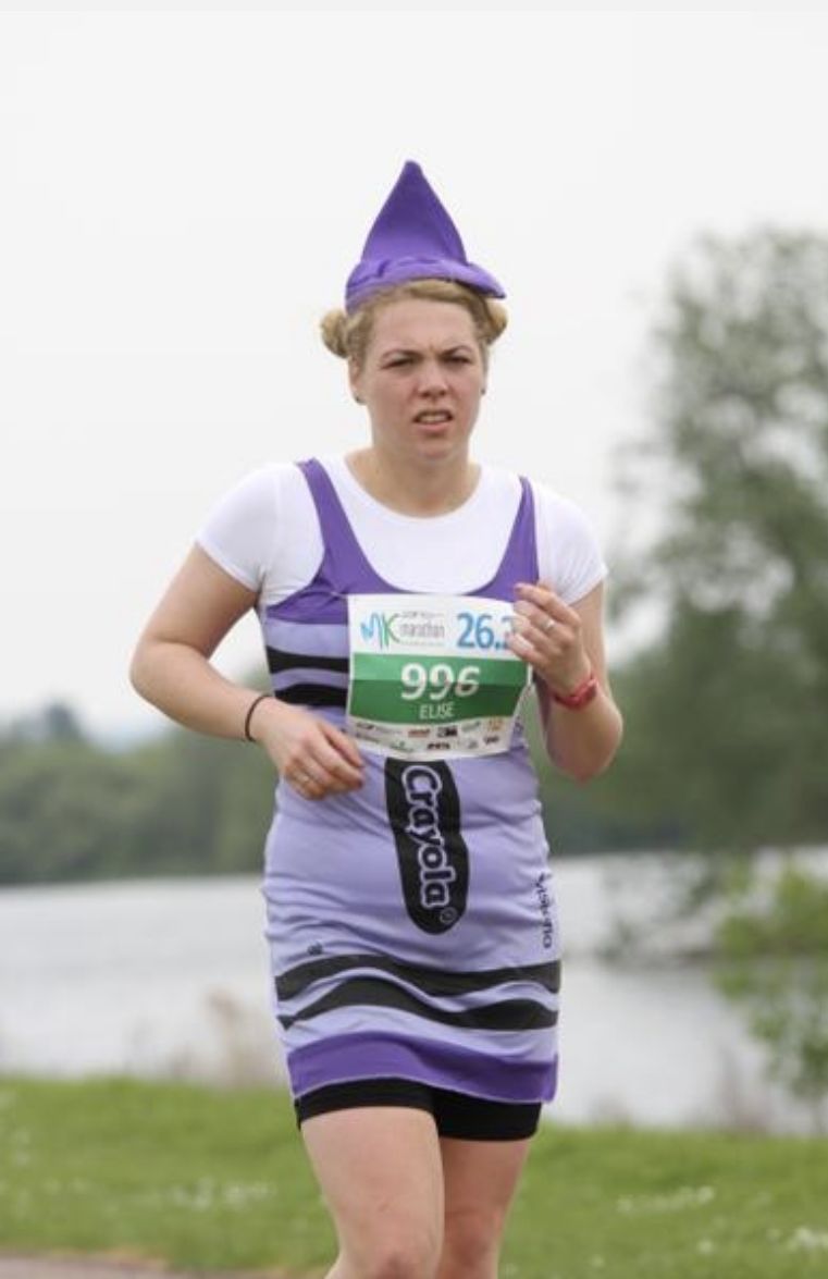 Elise, a white woman with blonde hair, running dressed as a purple crayon.