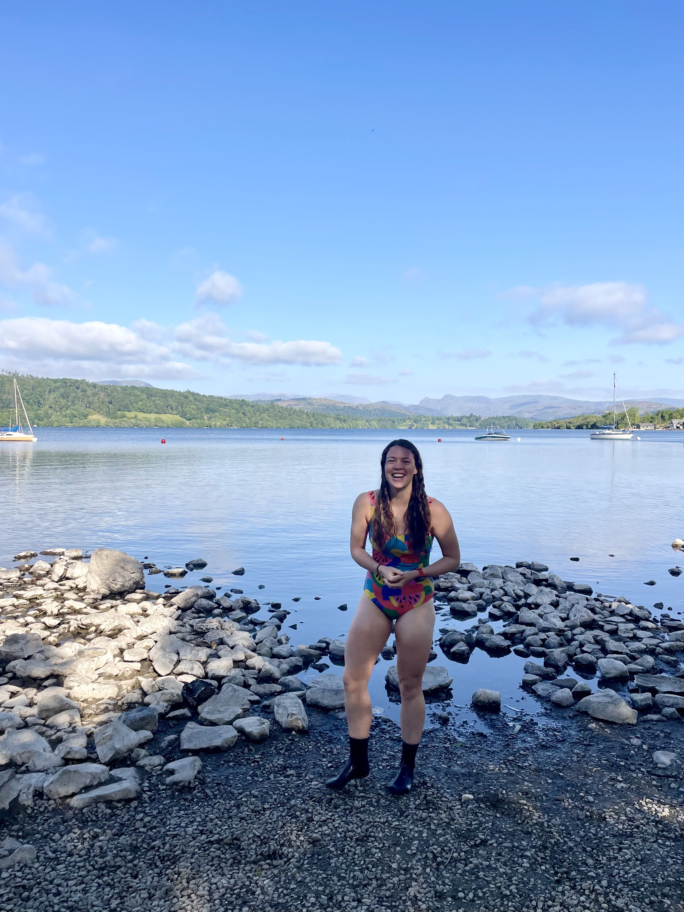 Elise smiling in a multicoloured swimming costume in front of a lake