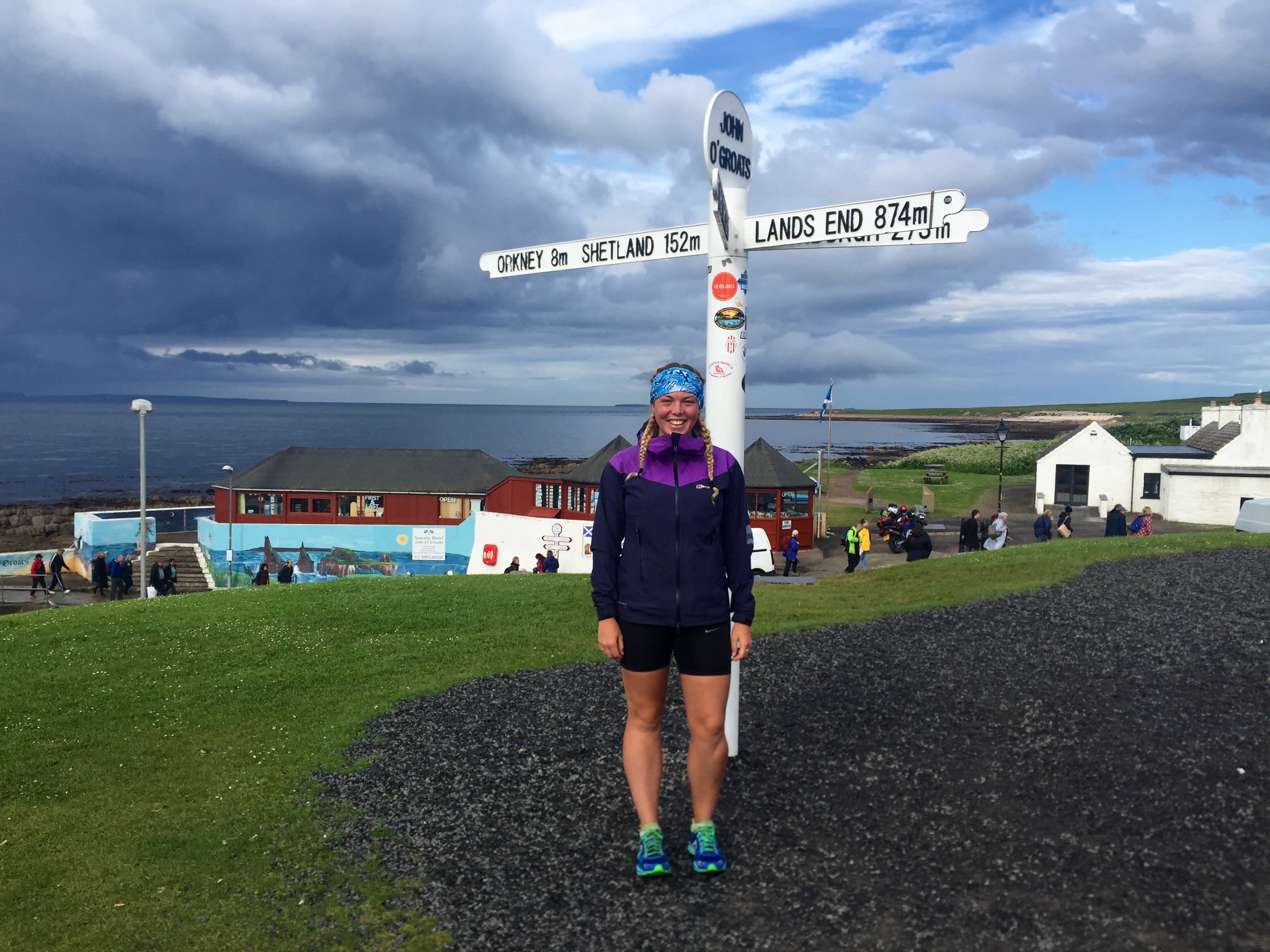 Elise in a purple coat smiling at the John O'Groats sign