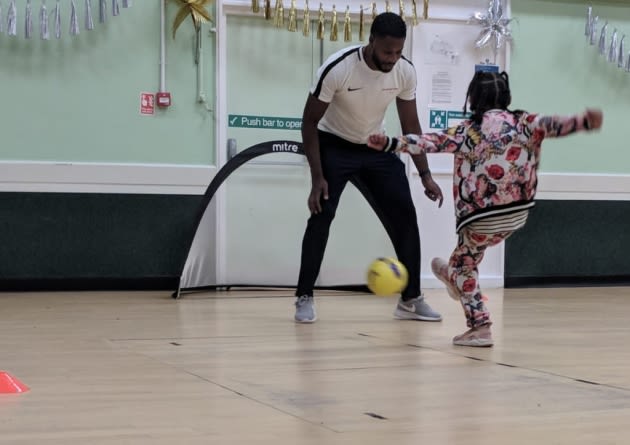 A little girl kicking a football towards Ola Williams.