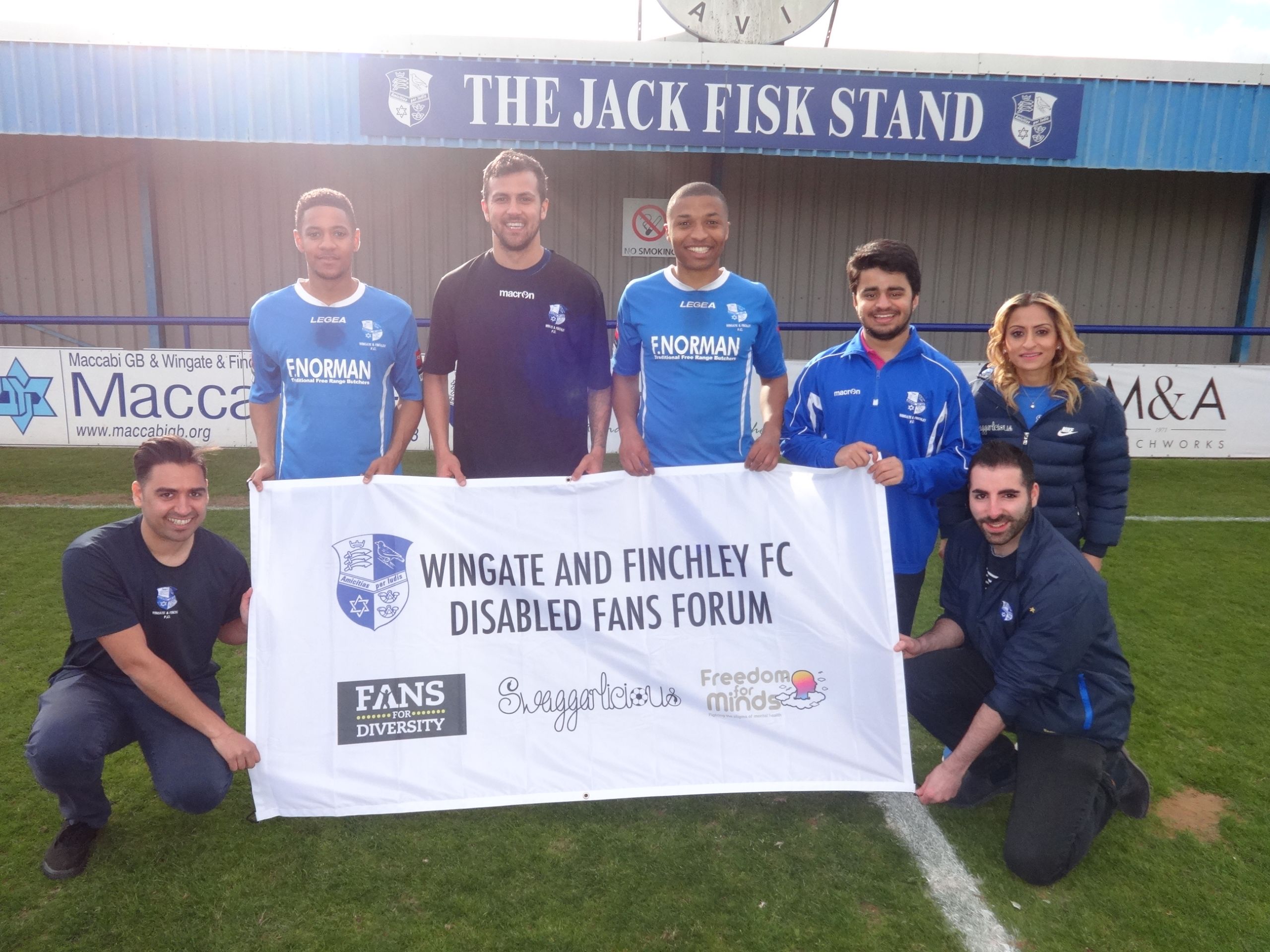 Manisha Tailor MBE of Swaggarlicious LTD proudly displaying the Wingate & Finchley Disabled Fans Forum banner with members of the first team and press team.