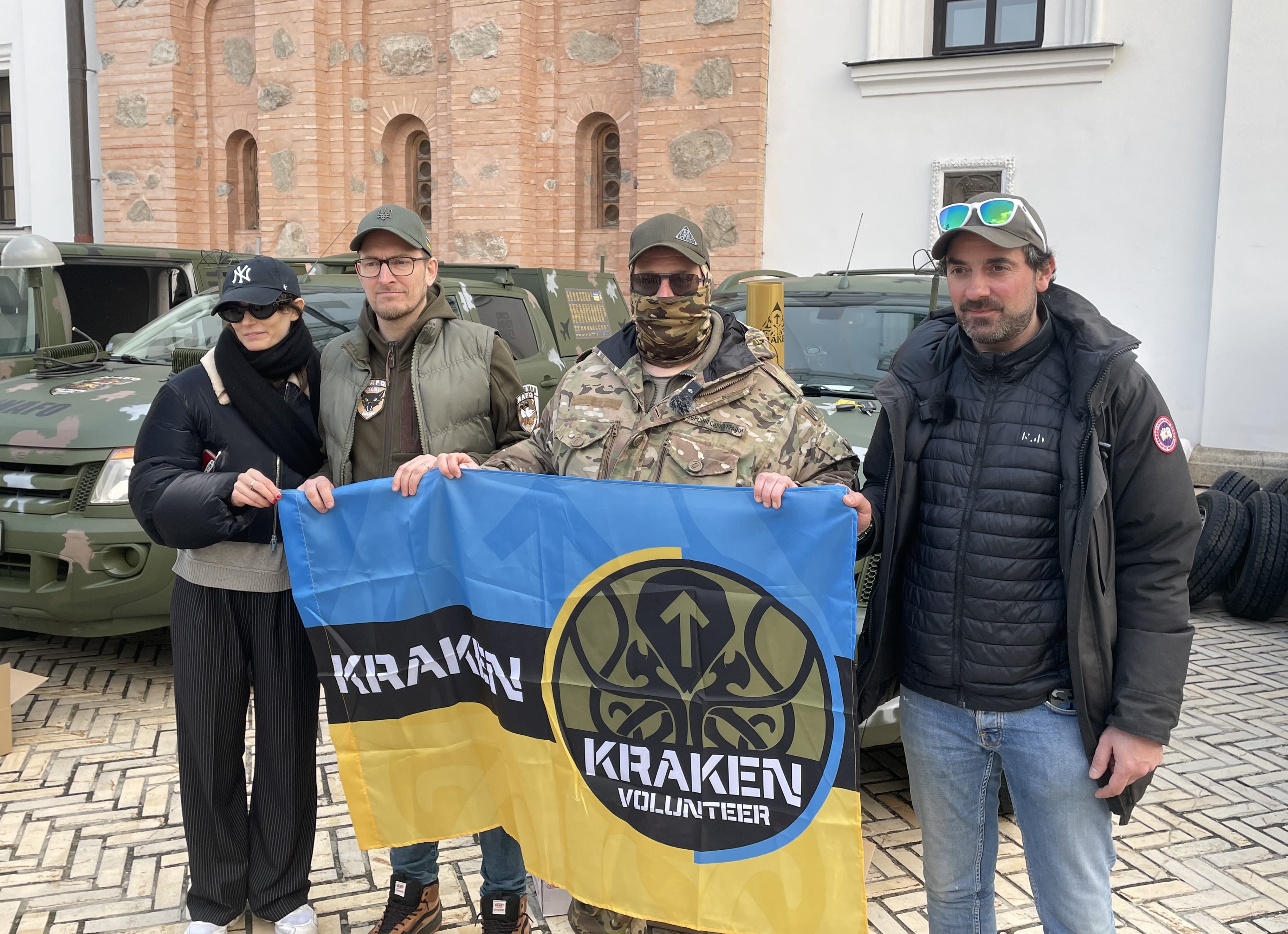 Soldiers posing with a unit flag and two drivers.