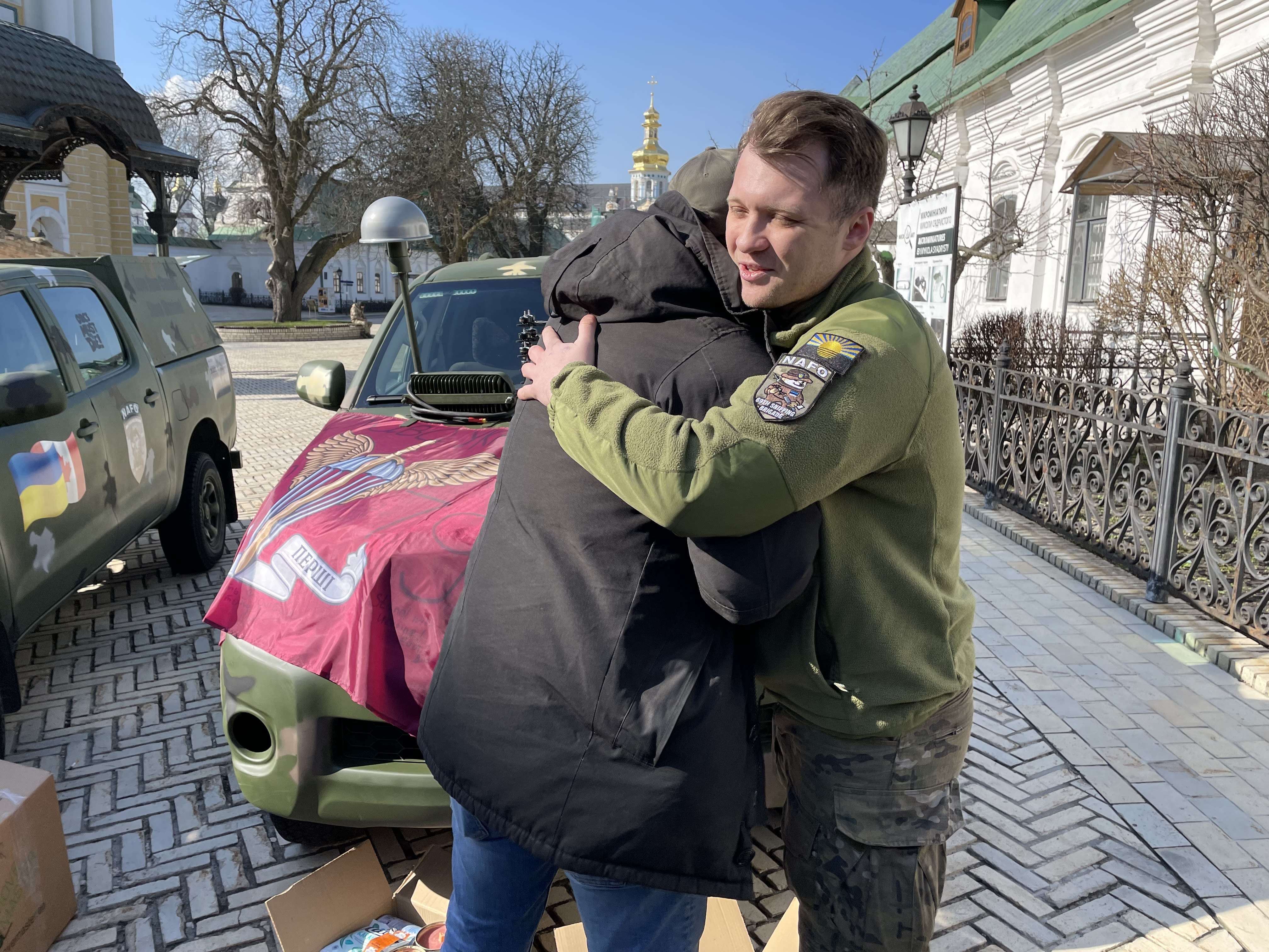 Two men hug in front of a vehicle.