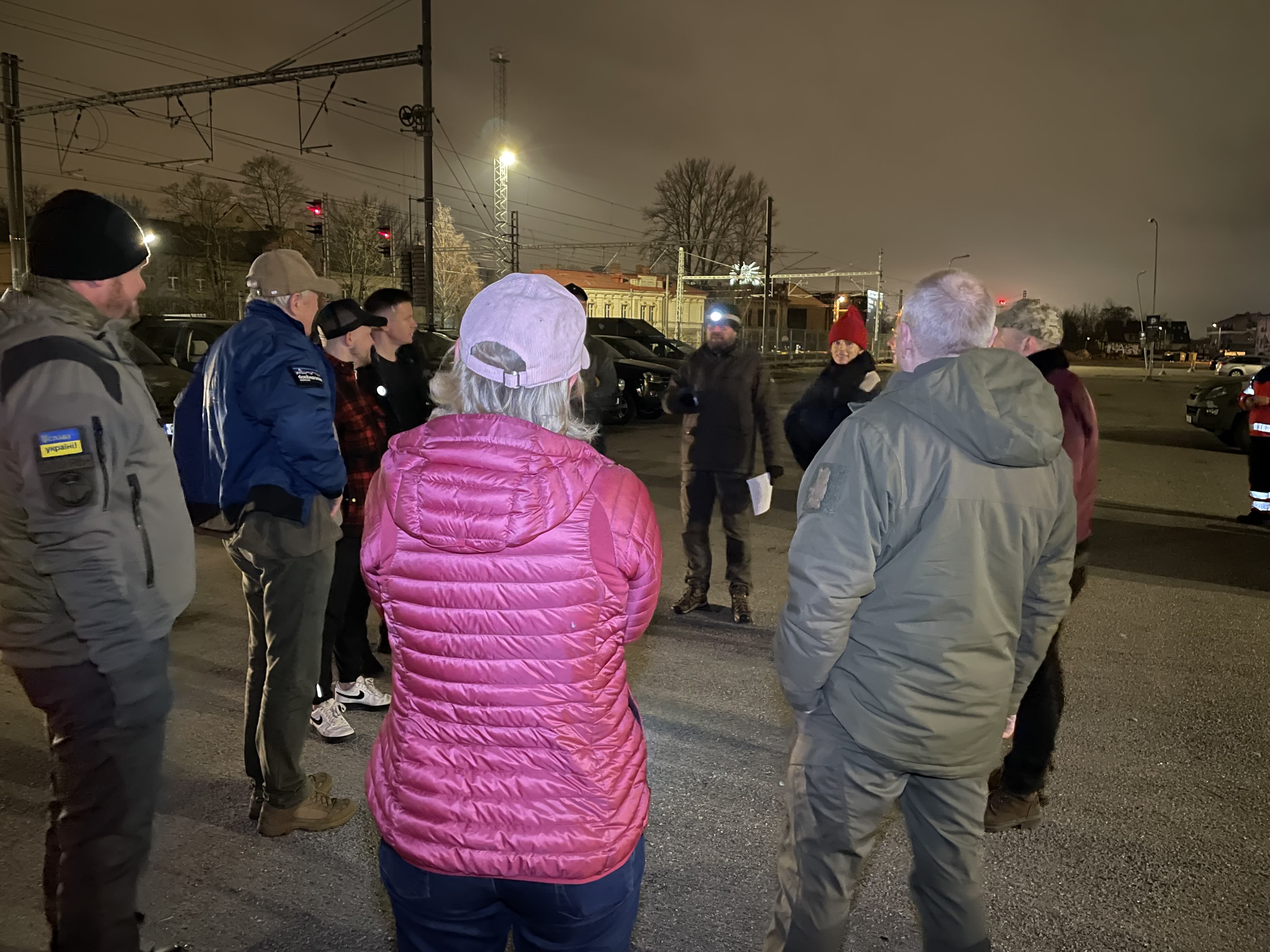 People standing in a car park in the early hours of the morning being briefed.